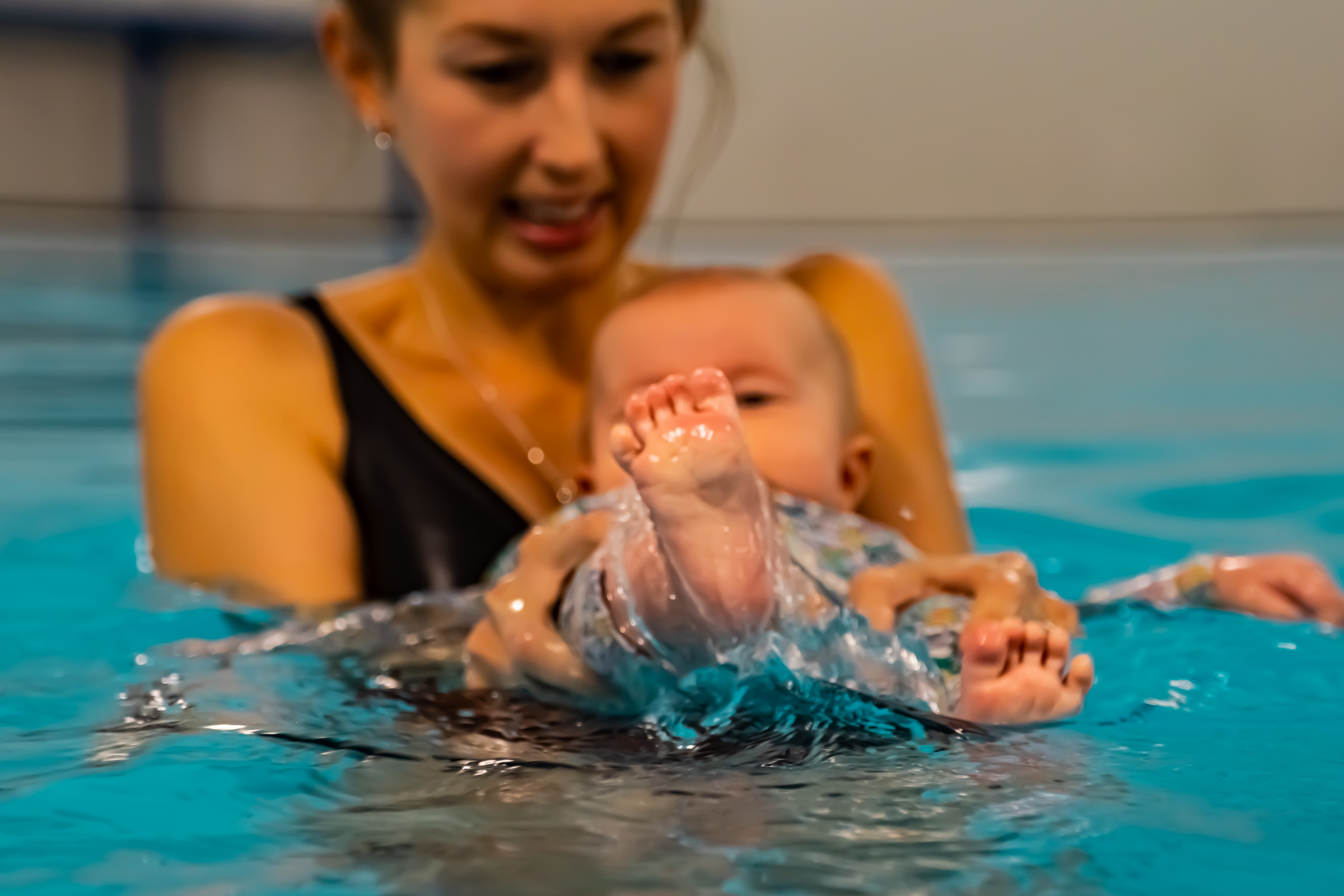 A mum supports her baby in the swimming pool as they lie back and kick their legs
