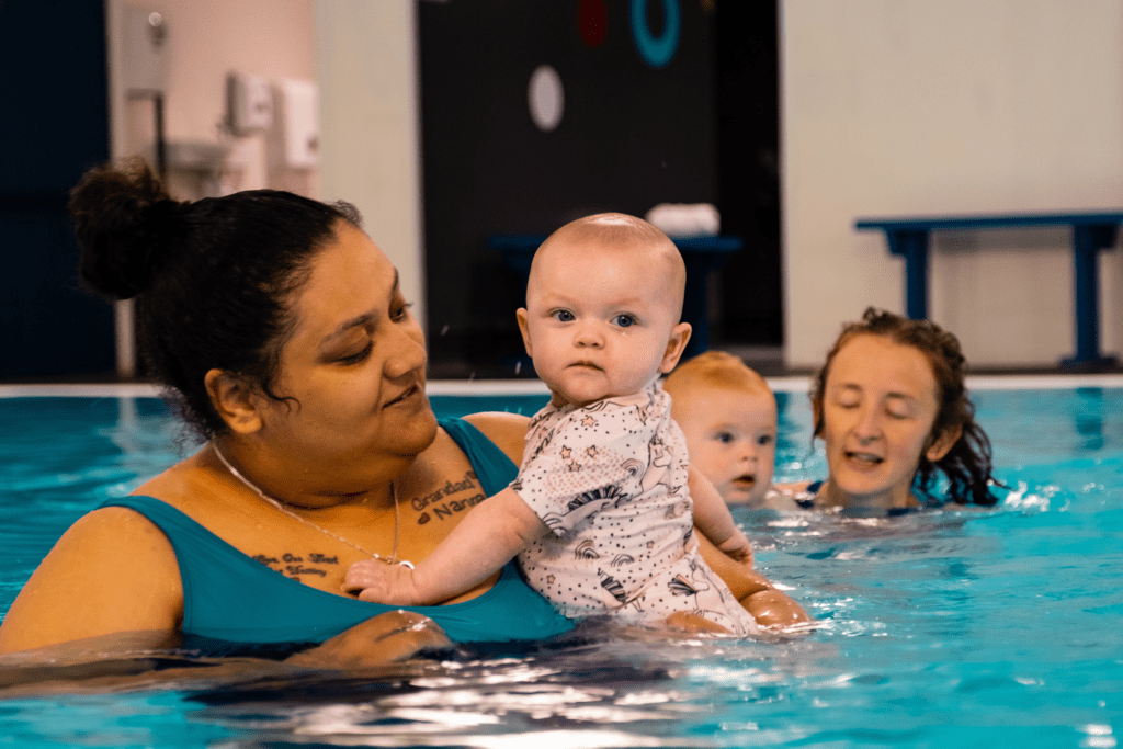 A mum holds her baby in the swimming pool as they enjoy a baby swimming lesson
