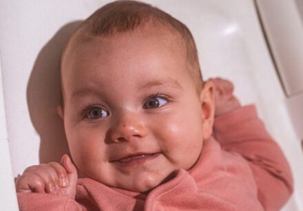 A baby dressed in pink lies on a changing table and smiles at the camera