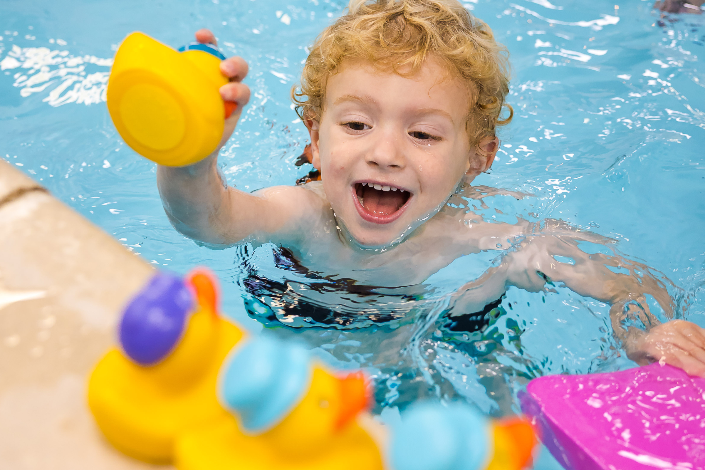 A young boy smiles and places a rubber duck on the side of the swimming pool