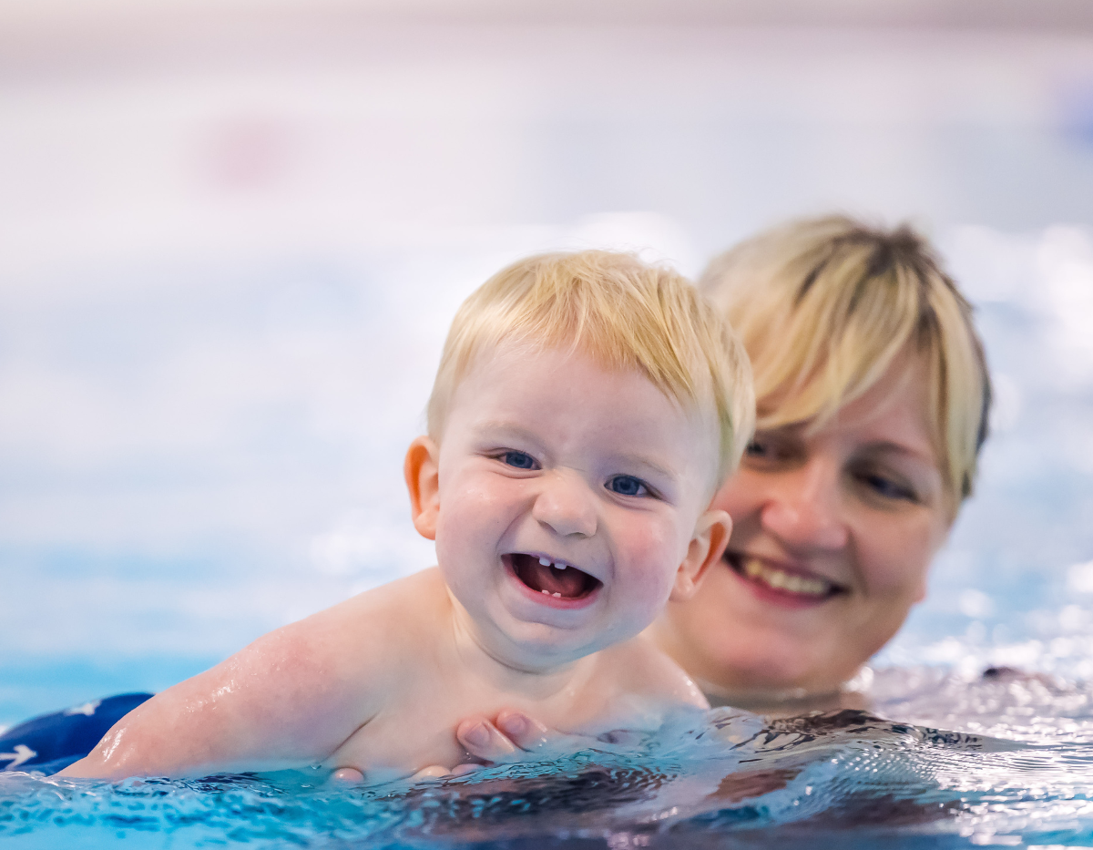 A toddler and mum move through the swimming pool together