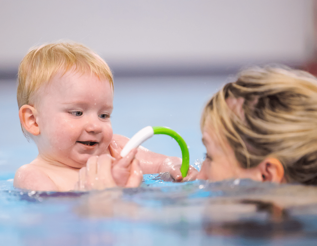 A young child looks at his mum through a hoop in the swimming pool