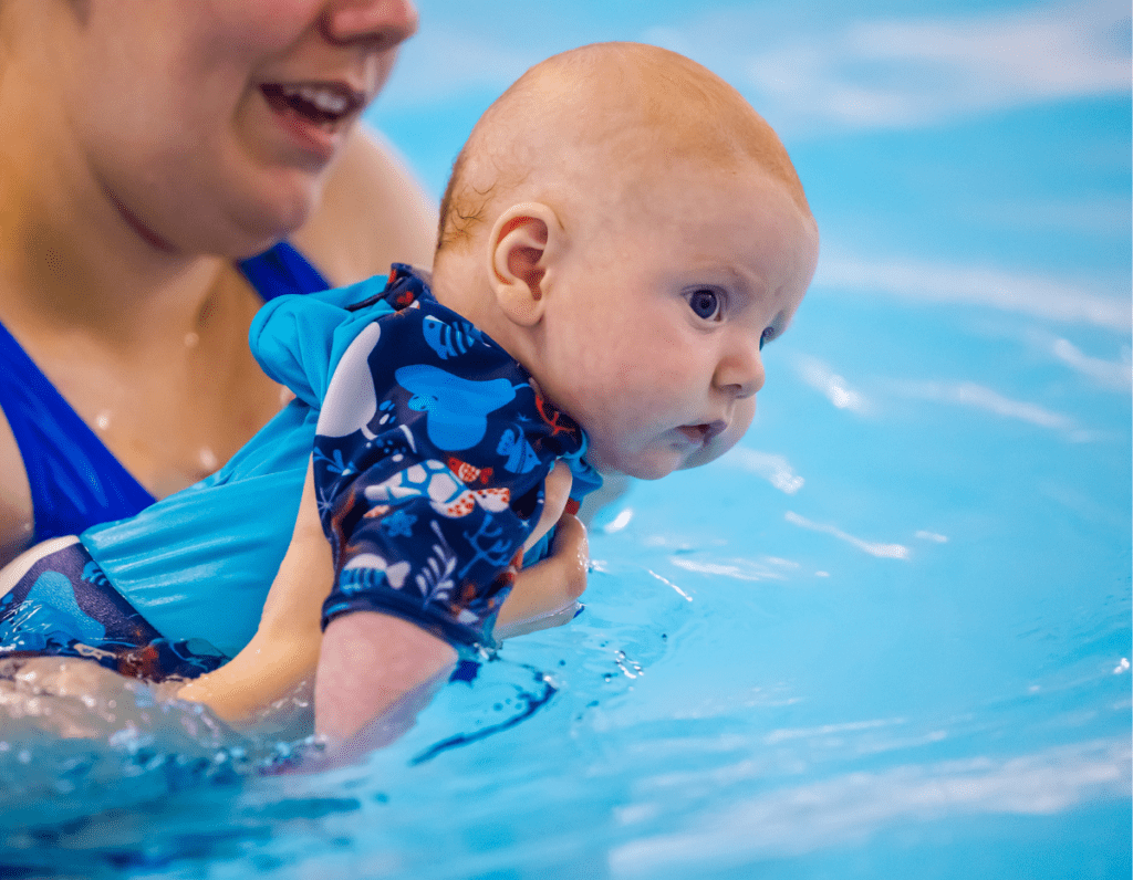 A young baby is guided around the swimming pool by their mum