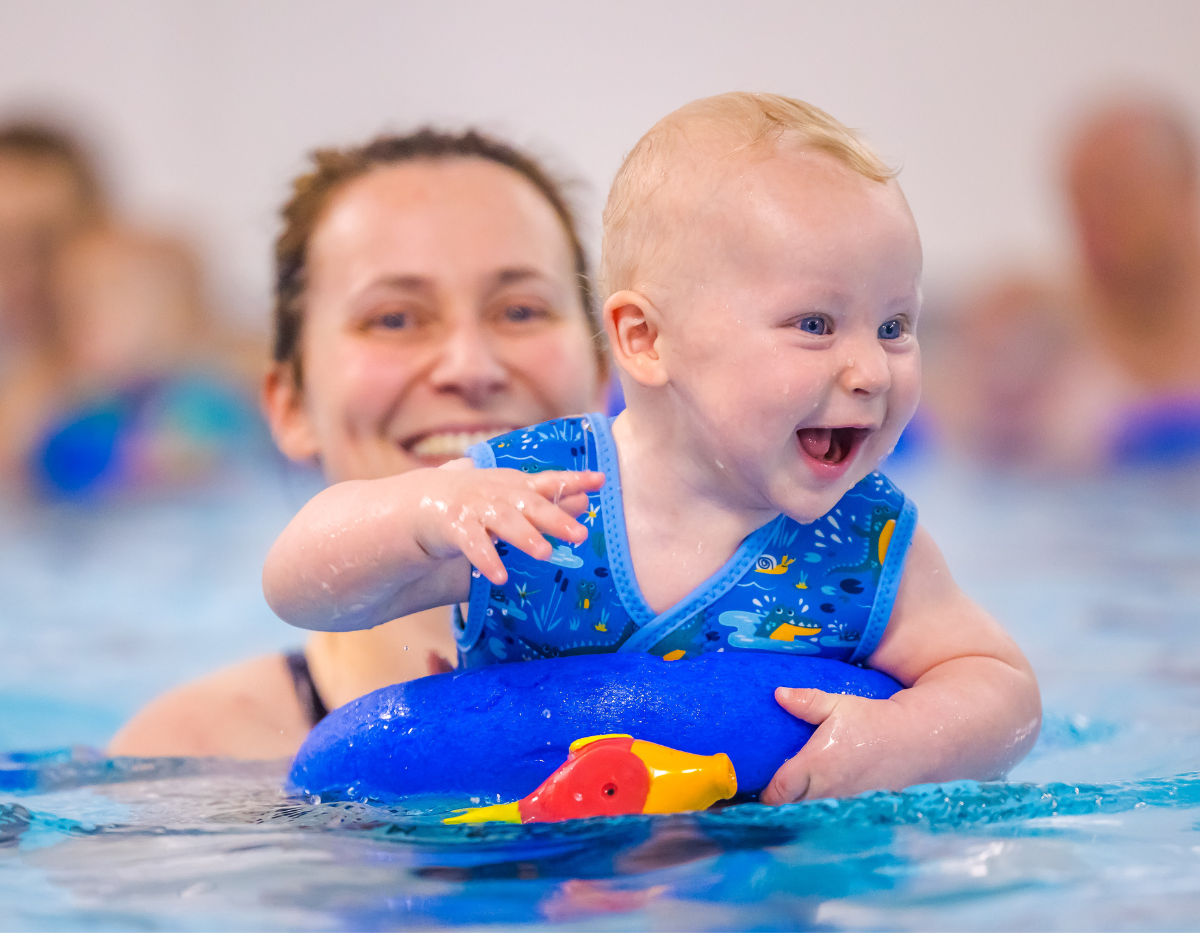 A baby smiles and laughs in the pool while with his mum