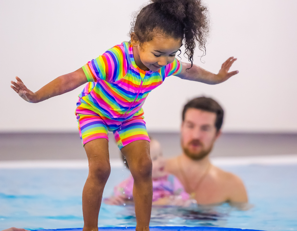 A young girl stands and balances on a float in the swimming pool
