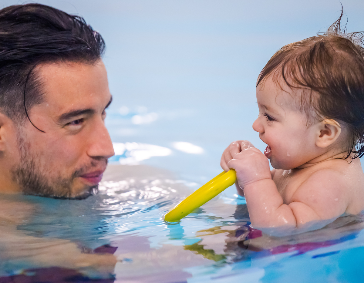 A baby and dad smile at each other in the swimming pool