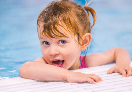A young girls looks at the camera while holding on to the side of the swimming pool